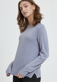 Svijetloplavi dugi rukav sv sweater s okruglim izrezom, rebrastim manžetama i bočnim prorezima na rubu. Napravljen od mekog materijala s glatkom teksturom.