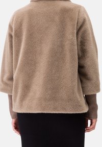 Top de tela suave color beige con un corte relajado, hombros caídos y mangas tres cuartos. Puños acanalados en un tono marrón más oscuro.