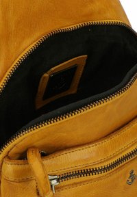 Gele leren rugzak interieur met zwarte stofvoering, uitgerust met een bovenrits, een rits voorvak en een gelabelde leren patch.