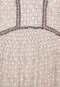 Tissu avec un motif de petits losanges rouges et verts sur fond beige et des lignes décoratives de couture rouges et vertes.
