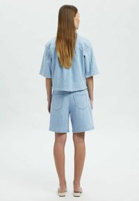 Chaqueta de mezclilla azul claro con mangas cortas, combinada con pantalones cortos a juego. Ambos tienen un ajuste casual y cuentan con bolsillos traseros. Textura suave.