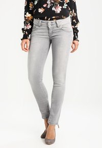 Šedé skinny jeans s hladkým povrchem, středně vysokým pasem a designem s pěti kapsami, doplněné černou blůzkou s květinovým vzorem.