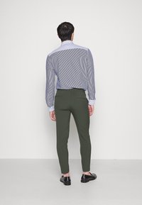 Mans bakåtblick iklädd en blå- och vitrandig skjorta, slim fit olivgröna byxor och svarta skor, med långa ärmar och snäv passform.