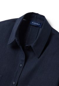 Navy blue linen shirt with a classic collar, featuring a button-down front and a small, branded label. Textured fabric with a smooth finish.