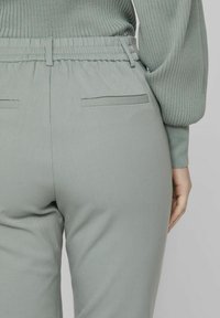 Vaaleanvihreät housut, joissa on sileä rakenne, joustava vyötärönauha ja kaksi takataskua. Ominaisuuksiin kuuluu muotoiltu leikkaus ja istuva malli.