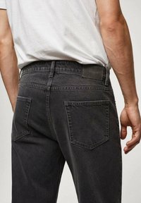 Jean en denim gris foncé à coupe droite, avec une pièce en cuir à la ceinture et deux poches arrière avec des détails cousus.