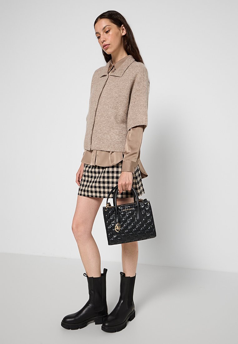 Pull en tricot beige à manches courtes, blouse beige, mini-jupe à carreaux, bottines en cuir noires et un sac à main noir à motif avec des accents dorés.