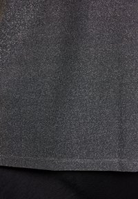 Zbliżenie na ciemnoszary, fakturowany materiał złożony na gładkim, czarnym materiale, podkreślające kontrast wykończeń tkanin.