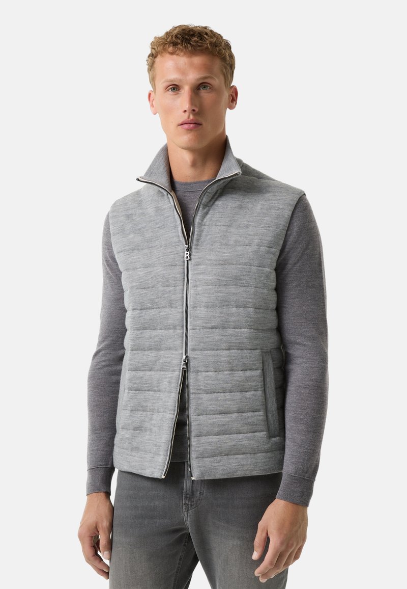 Graue Steppweste mit einem Reißverschluss auf der Vorderseite, hohem Kragen und gestepptem Muster. Weicher Stoff, taillierte Passform und seitliche Taschen. Über einem grauen Sweater getragen.