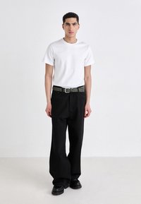 Hvid crew neck t-shirt, afslappede sorte bukser, struktureret grøn bælte og kraftige sorte sko. Simpel, minimalistisk stil.
