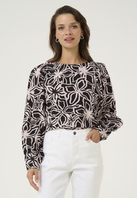 Schwarze und rosa blumenmusterte Bluse mit langen Ärmeln und einem Boot-Ausschnitt, kombiniert mit weißen Jeans. Glatte Stofftextur.