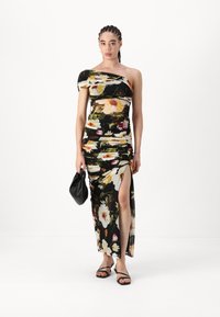 Musta kukkakuosiset mekko, jossa on yksi olka, rypytetty muotoilu, reiden korkuinen halkio ja vaalean kukkakuvio. Malli pitää mustaa clutch-laukku ja käyttää mustia sandaaleja.