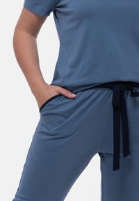 Sininen puuvillainen lounge-setti, jossa on rento malli, lyhyet hihat, sivutaskut ja kiristysnauha, jossa on kontrastina tummansinisiä yksityiskohtia.