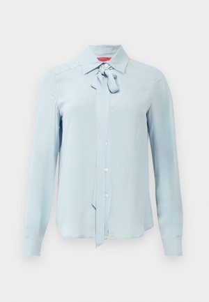 Blouse bleu clair à manches longues avec un devant à boutons, un col pointu et un nœud en tissu noué au niveau du cou.
