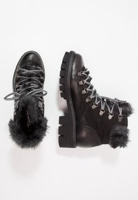 Botas de senderismo negras hechas de cuero y gamuza, con un borde de piel sintética, cordones metálicos y una suela gruesa con agarre para tracción.