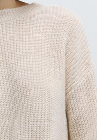 Maglione lavorato a maglia in morbido beige, con vestibilità ampia, motivo testurizzato e scollatura a coste. Tessuto liscio di peso medio con leggero effetto elasticizzato.