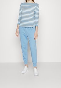 Chemise à manches longues rayée bleu et blanc associée à un pantalon de survêtement bleu clair et des baskets blanches. Tissu lisse, coupe décontractée, et poignets élastiques.