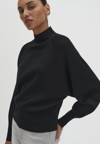 Pullover nero a maglia con collo alto e maniche a sbuffo. Presenta dettagli a coste sui polsini e sull'orlo. Texture liscia, design aderente.