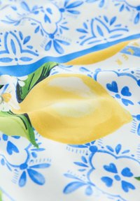Tissu imprimé de citrons avec des citrons jaunes vifs, des feuilles vertes et des motifs floraux bleus sur un fond blanc ; texture douce.