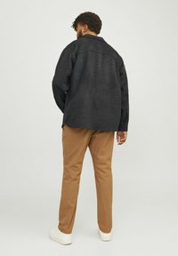 Black wool shirt jacket with a relaxed fit, accompanied by light brown chinos and white sneakers. The jacket features a collar and visible seams.