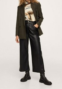 Ruskea ruudullinen kaksirivinen bleiseri marmorikuvioidun, istuvan paidan päällä. Mustat leveälahkeiset nahkahousut ja massiiviset mustat saappaat täydentävät asua.