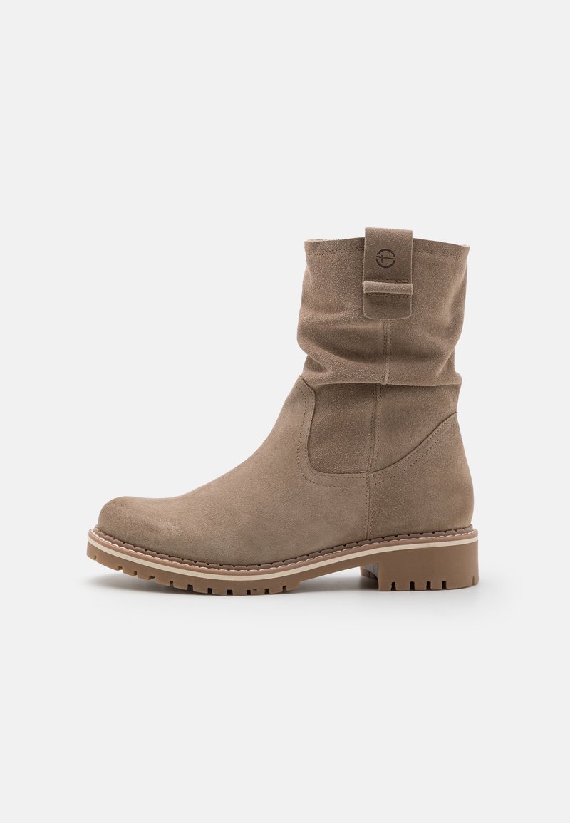 Botte mi-mollet en daim beige avec un bout arrondi, une languette avec logo, une semelle cousue et un petit talon bloc sur fond blanc.