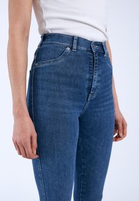 Höga blå denimjeans med en slät textur, femficksdesign och synlig söm längs sömmarna och midjebandet.