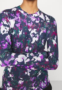 Långärmad atletisk tröja med en mörk marinblå bas och ett färgglatt blommönster samt abstrakt mönster i lila, grönt och vitt.