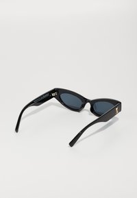 Occhiali da sole neri a forma di occhio di gatto con lenti scure e montatura lucida. Presentano dettagli in oro sulle aste e un design affusolato per una forma distintiva.