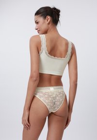 Set de lenjerie de culoare galben deschis, format dintr-un bralet din material ribat cu dantelă la margine și chiloți din dantelă transparentă asortați, cu motive florale și margini zimțate.