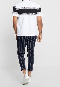 Bílý tričko s černými a hadími pruhy, v kombinaci s pruhovanými námořnickými kalhotami. Outfit doplňují bílé tenisky.