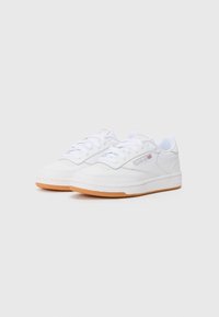 White sneakers made of leather and mesh, featuring a smooth finish, classic lace-up design, and gum rubber outsole with logo accents.