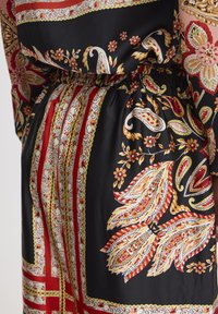 Zijden jurk met een zwarte basis, voorzien van rode en gele paisleypatronen, bloemen details en een elastische taille met gestreepte accenten.