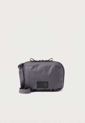 Petit sac bandoulière gris foncé compact avec sangle réglable et double fermeture éclair, arborant le logo The North Face à l'avant.