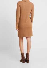 Robe tricotée côtelée beige avec col roulé et manches longues, assortie à des bottines cheville en cuir serpent marron avec un talon large.