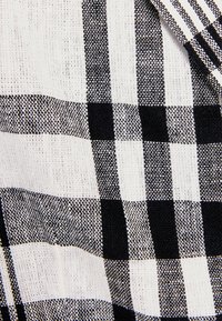 Tissu à carreaux noir et blanc avec une surface texturée ; présente de grands carrés et des détails fins dans le motif de tissage.