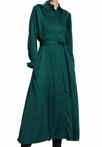 Robe en satin vert avec col, manches longues, ceinture à la taille et poches latérales. Silhouette fluide avec une texture lisse.
