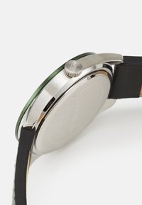 Montre en acier inoxydable avec une lunette verte, un bracelet en cuir noir, une couronne argentée et un dos lisse, présentant des détails gravés.
