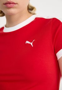 Red short-sleeve t-shirt with white collar and sleeve accents. Features a white Puma logo on the left chest area. Smooth fabric texture.