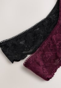 Fekete és sötétlila csipkés fehérnemű, virágmintákkal, egy világos felületen kiterítve.