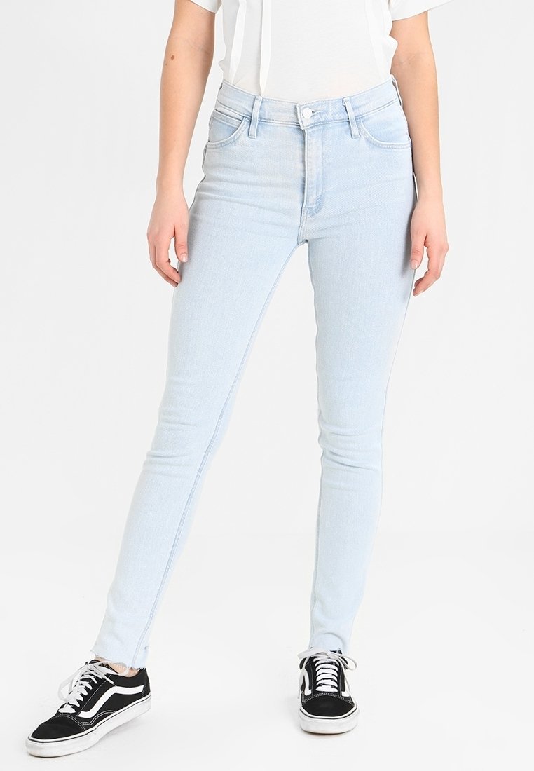 Jeans ajustados de color azul claro hechos de denim con un diseño clásico de cinco bolsillos. Llevados con una camiseta blanca y zapatillas negras.