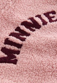 Gros plan d'un tissu rose texturé avec des fibres douces en boucles et des lettres rouge foncé partiellement visibles formant une partie d'un mot.