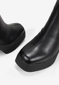 Bottines en cuir noir avec une semelle à plateau texturée noire, dotées d'une finition lisse et d'un design à bout rond.