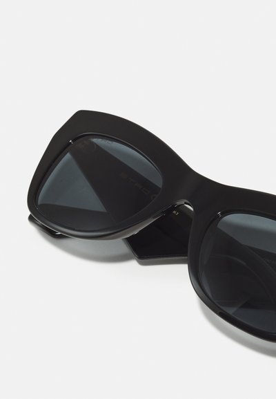 Occhiali da sole neri oversize con design angolare, lenti scure e telaio in plastica liscia. Marchio ben visibile sulla parte interna del braccio.