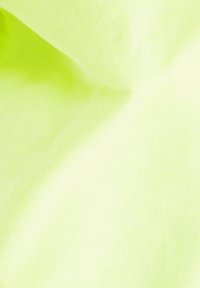 Tela amarilla neón con una textura suave, que muestra un brillo sutil y ligeras arrugas, típico del material de algodón ligero.
