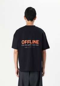 Tricou oversized negru cu text portocaliu pe spate care spune "OFFLINE PENTRU MOTIVE PRIVATE." Fabricat din bumbac, are mâneci scurte.