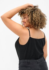 Zwarte camisole-top met dunne bandjes, zachte stof en een losse pasvorm. Draagt in combinatie met hoge taille zwarte jeans, wat een casual ontwerp laat zien.