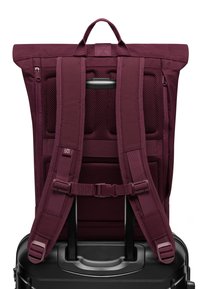 Zaino marrone con spalline in rete imbottita e maniglia superiore. Include una tasca laterale con zip e un attacco per il manico della valigia. Tessuto resistente.