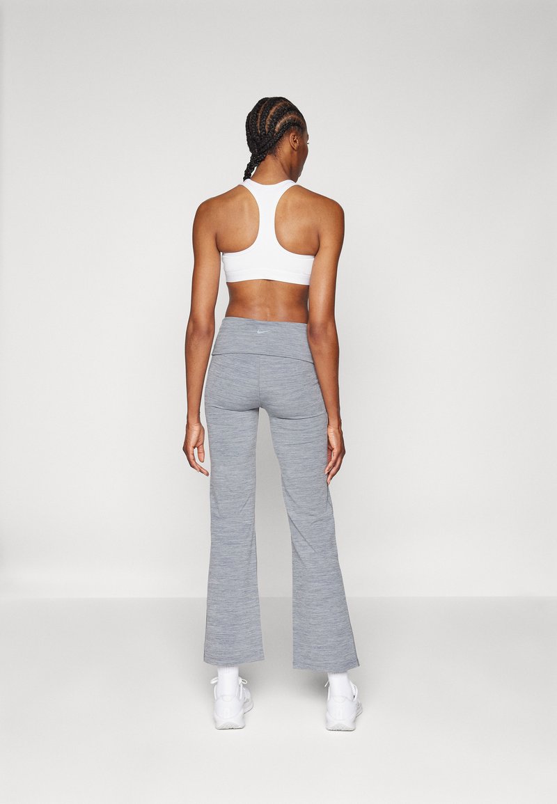 Weißer Sport-BH mit Racerback-Design, kombiniert mit hellgrauen, ausgestellten Leggings, die über eine glatte Textur und einen subtilen Stretch verfügen. Weiße Sneaker sind sichtbar.