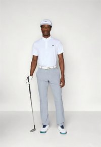 Hvit polotrøye med svart logo, lysegrå bukser, hvite sko med blå detaljer, holder en golfkølle, iført hvit caps og hanske.